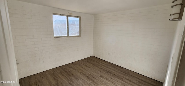 unfurnished room featuring brick wall and dark hardwood / wood-style flooring