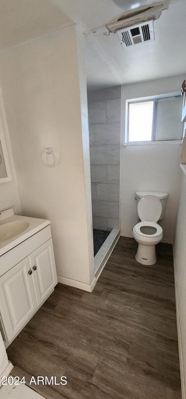 bathroom with tiled shower, toilet, vanity, and wood-type flooring