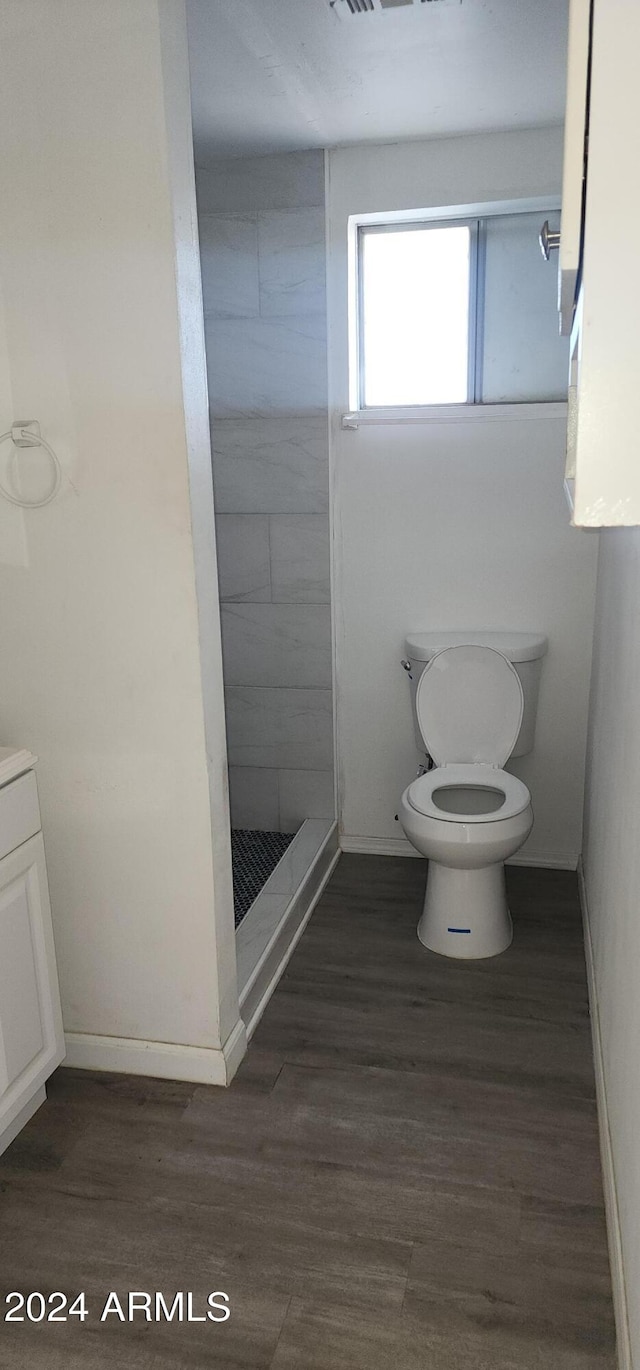 bathroom featuring wood-type flooring, vanity, toilet, and tiled shower