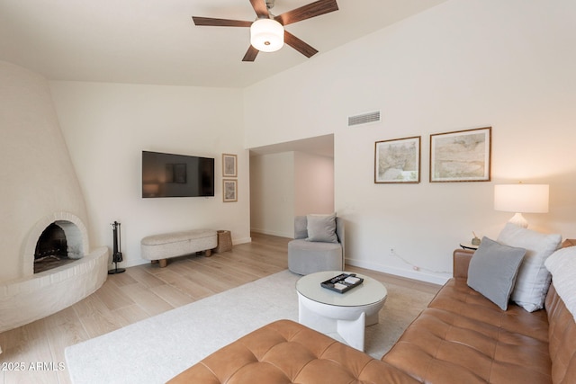 living area featuring a ceiling fan, vaulted ceiling, baseboards, and a brick fireplace