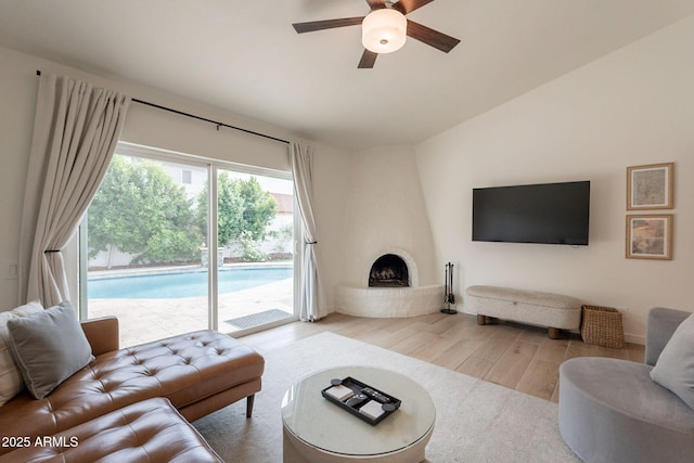 living room featuring wood finished floors, ceiling fan, vaulted ceiling, and a large fireplace