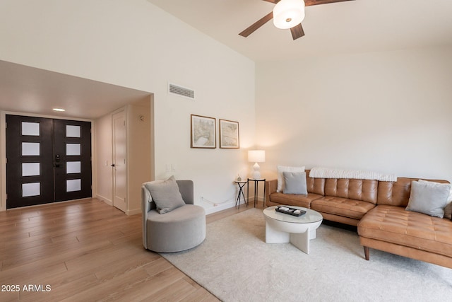 living area featuring light wood-style floors, a ceiling fan, baseboards, and a high ceiling