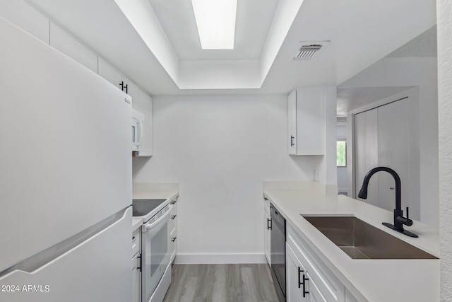 kitchen with white appliances, sink, light hardwood / wood-style floors, and white cabinets