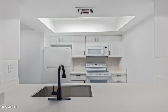 kitchen with a tray ceiling, white appliances, sink, and white cabinets