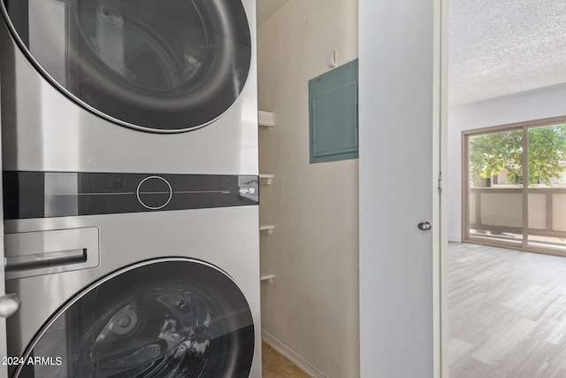 laundry area with electric panel, light hardwood / wood-style flooring, stacked washer and dryer, and a textured ceiling