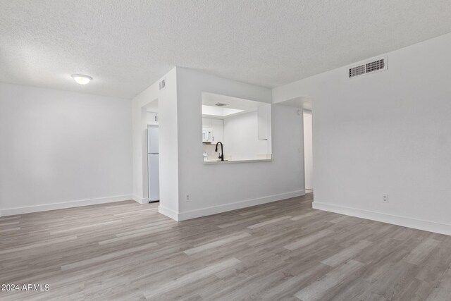 unfurnished living room featuring a textured ceiling, sink, and light hardwood / wood-style floors