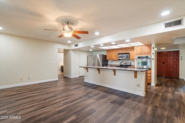 kitchen with dark wood-style flooring, a kitchen breakfast bar, visible vents, appliances with stainless steel finishes, and a sink