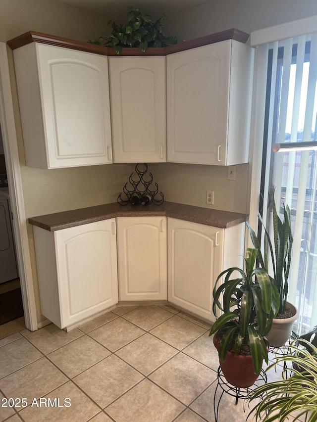 kitchen with washer / dryer, light tile patterned floors, and white cabinets