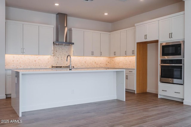 kitchen featuring oven, white cabinetry, wall chimney range hood, and built in microwave