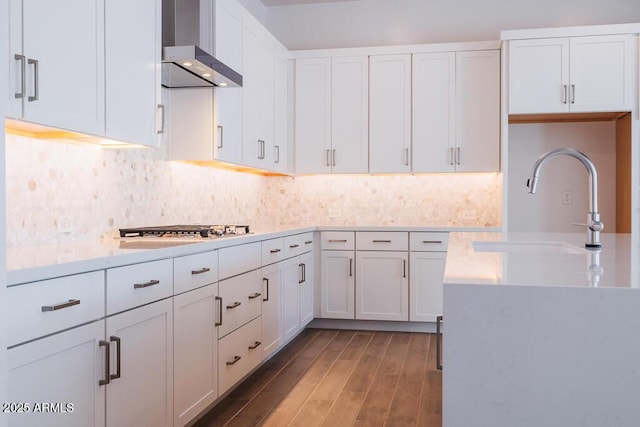 kitchen featuring stainless steel gas stovetop, sink, wall chimney exhaust hood, tasteful backsplash, and white cabinetry