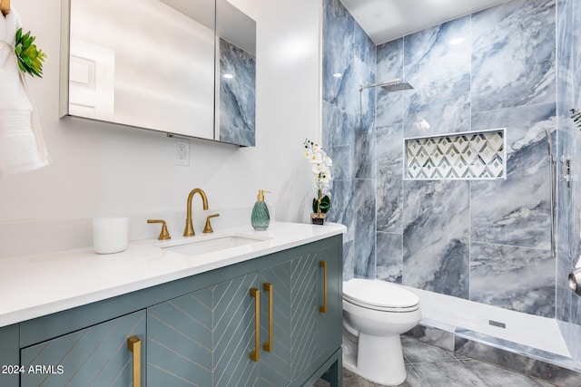 bathroom featuring toilet, a tile shower, vanity, and tile patterned floors