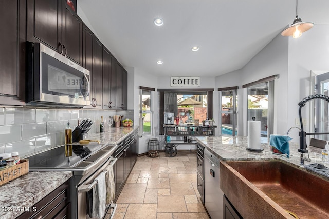 kitchen with sink, decorative backsplash, light stone countertops, appliances with stainless steel finishes, and dark brown cabinets