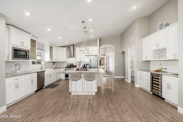 kitchen featuring wine cooler, white cabinetry, appliances with stainless steel finishes, a kitchen island, and wall chimney range hood