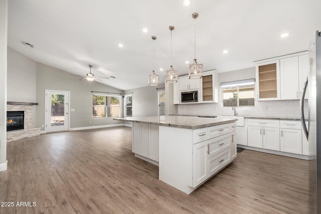 kitchen with pendant lighting, stainless steel appliances, light stone countertops, white cabinets, and a kitchen island