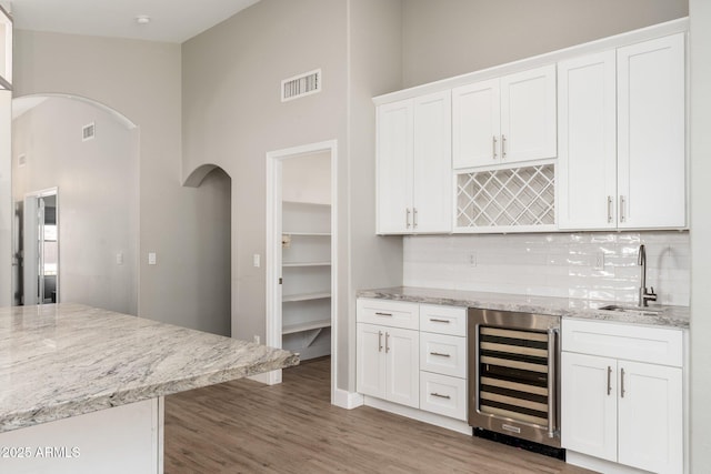 kitchen featuring sink, hardwood / wood-style flooring, wine cooler, light stone countertops, and white cabinets