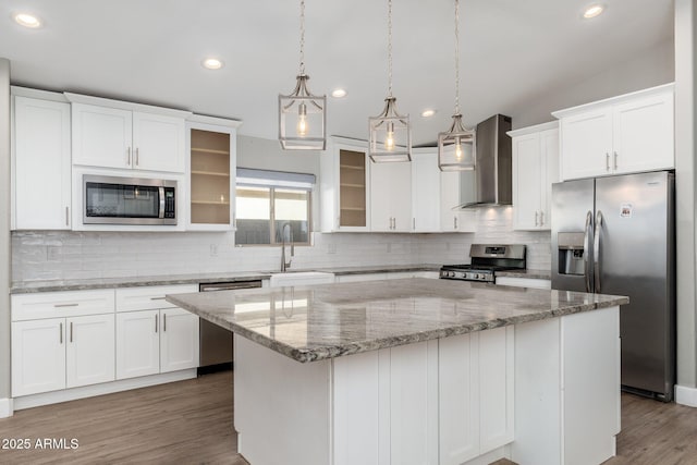 kitchen with wall chimney range hood, white cabinetry, hanging light fixtures, stainless steel appliances, and a center island