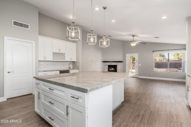 kitchen featuring white cabinetry, light stone counters, decorative light fixtures, a center island, and light wood-type flooring