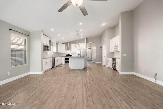 kitchen featuring a kitchen island, decorative light fixtures, white cabinetry, stainless steel appliances, and wall chimney range hood