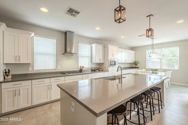 kitchen featuring visible vents, a kitchen bar, a sink, appliances with stainless steel finishes, and wall chimney range hood