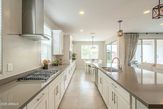 kitchen with visible vents, a sink, decorative light fixtures, appliances with stainless steel finishes, and wall chimney range hood