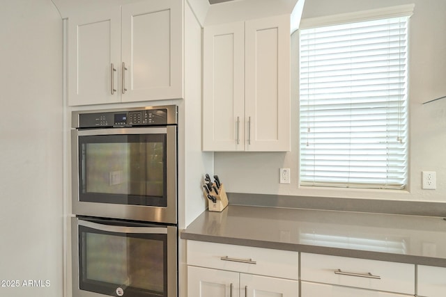 kitchen with white cabinetry, dark countertops, and stainless steel double oven