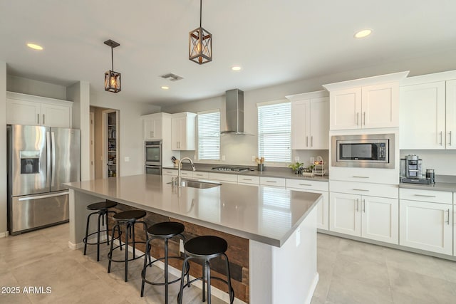 kitchen featuring visible vents, a sink, white cabinetry, stainless steel appliances, and wall chimney range hood