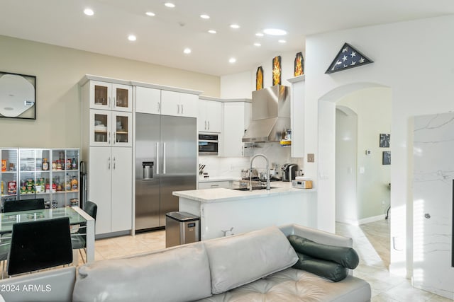 kitchen with backsplash, white cabinets, wall chimney range hood, appliances with stainless steel finishes, and kitchen peninsula