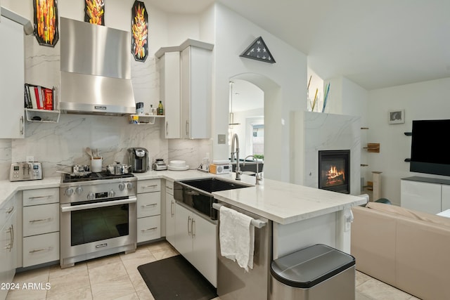 kitchen featuring range hood, kitchen peninsula, decorative backsplash, a fireplace, and appliances with stainless steel finishes