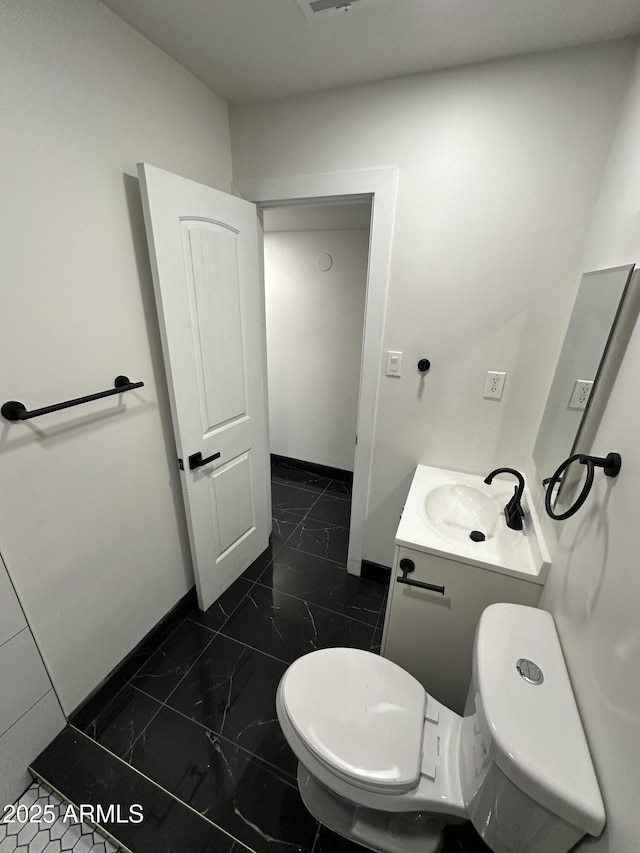 half bath with baseboards, marble finish floor, vanity, and toilet