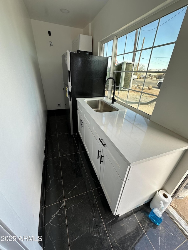 kitchen featuring a sink, marble finish floor, freestanding refrigerator, white cabinetry, and baseboards