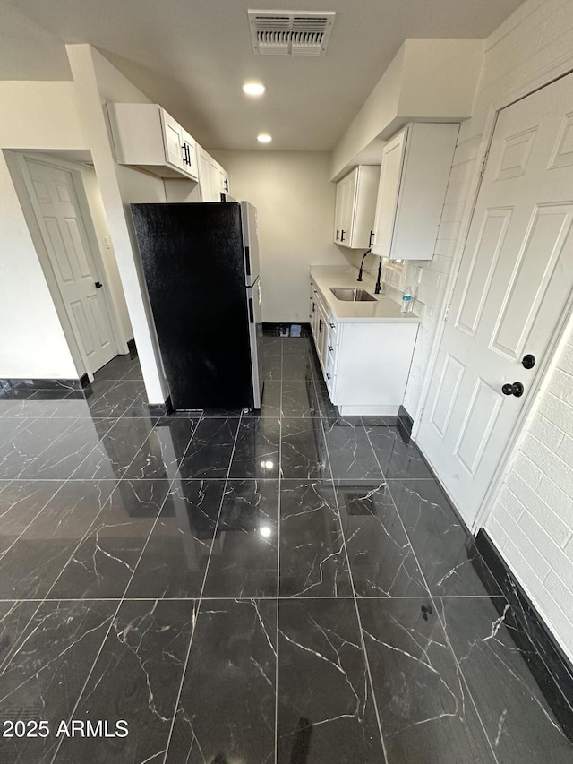 kitchen featuring freestanding refrigerator, baseboards, marble finish floor, visible vents, and a sink