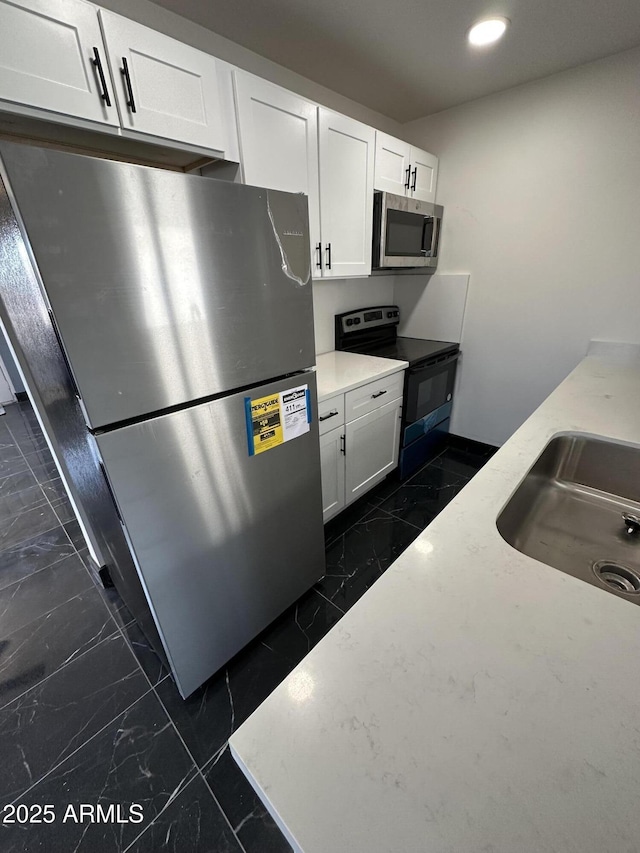 kitchen featuring a sink, stainless steel appliances, white cabinetry, and marble finish floor