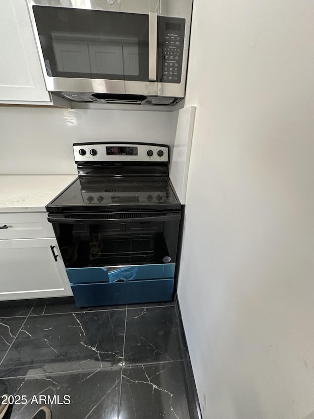 kitchen with white cabinetry, electric range oven, stainless steel microwave, light countertops, and marble finish floor