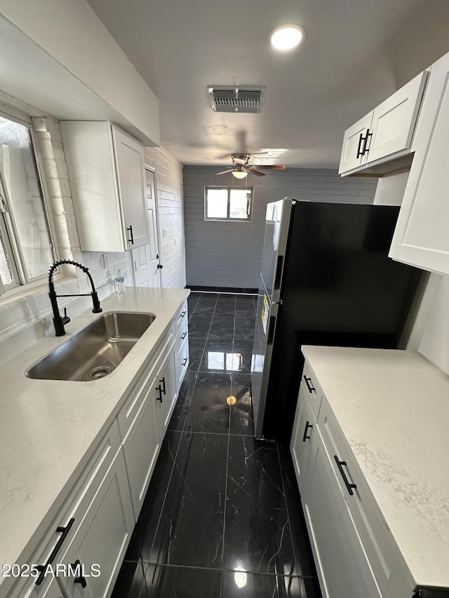 kitchen with a sink, marble finish floor, freestanding refrigerator, ceiling fan, and white cabinetry