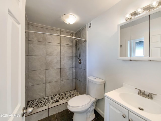 bathroom with toilet, a tile shower, and vanity