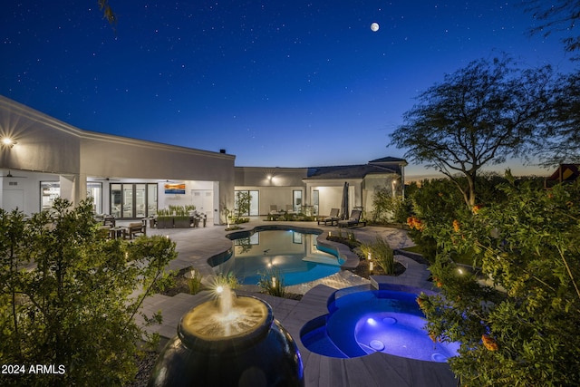 pool at dusk with an in ground hot tub, french doors, and a patio