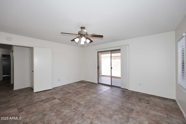 empty room with ceiling fan, baseboards, and stone finish flooring