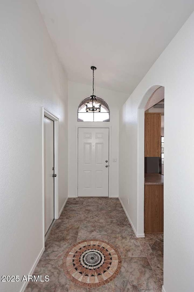 foyer entrance with arched walkways, baseboards, and lofted ceiling