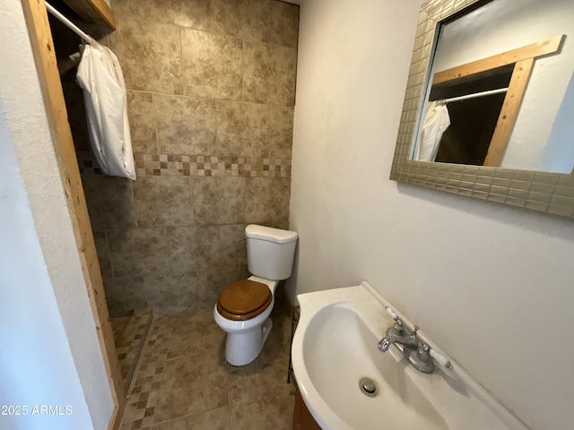 full bath featuring a tile shower, toilet, and a sink