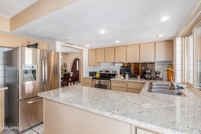 kitchen with backsplash, appliances with stainless steel finishes, light stone counters, cream cabinetry, and sink