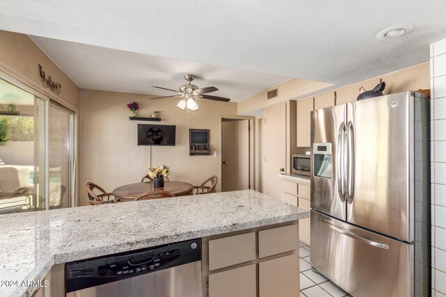 kitchen featuring stainless steel appliances, light stone countertops, a textured ceiling, light tile patterned floors, and ceiling fan