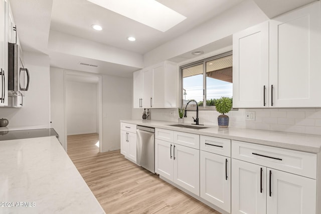 kitchen with white cabinetry, stainless steel dishwasher, a skylight, and sink