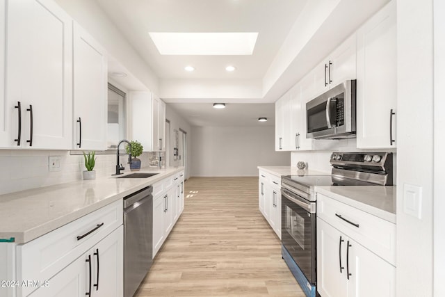 kitchen with a skylight, white cabinetry, sink, appliances with stainless steel finishes, and light wood-type flooring