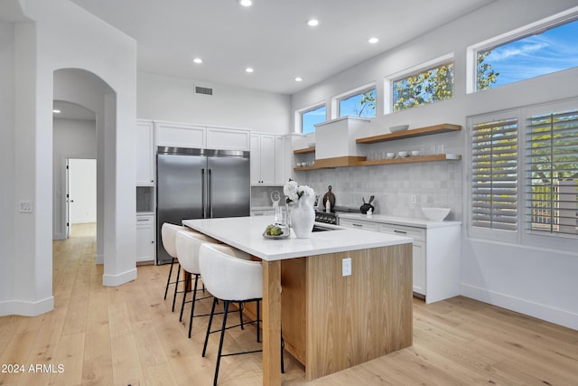 kitchen featuring white cabinetry, a breakfast bar area, a center island with sink, and stainless steel built in refrigerator