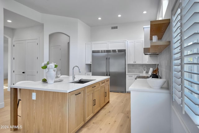 kitchen featuring light wood finished floors, tasteful backsplash, visible vents, a sink, and built in fridge