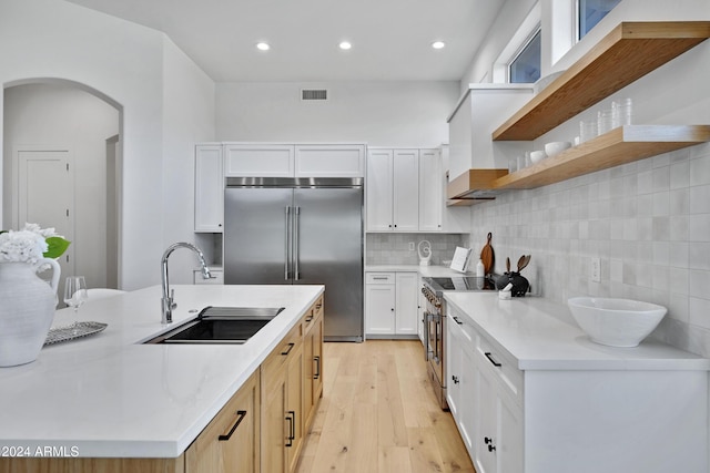 kitchen featuring sink, white cabinetry, tasteful backsplash, high end appliances, and light wood-type flooring