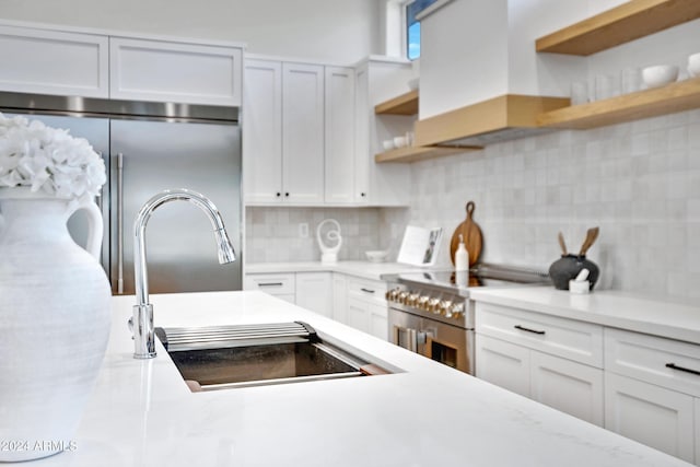 kitchen with premium range hood, sink, white cabinetry, high end appliances, and tasteful backsplash