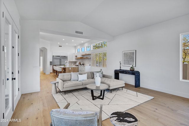 living room with arched walkways, visible vents, light wood-style floors, vaulted ceiling, and baseboards