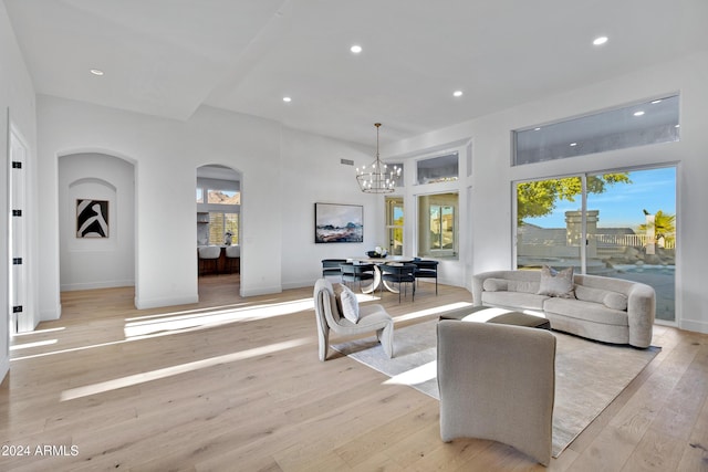 living area featuring baseboards, arched walkways, light wood-style floors, a notable chandelier, and recessed lighting