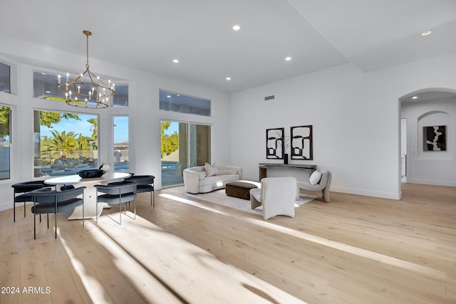 living room featuring an inviting chandelier, a towering ceiling, and light hardwood / wood-style flooring